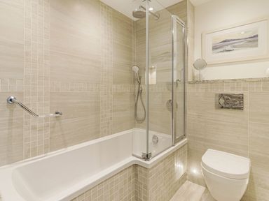 A bathroom with a bathtub shower screen and a wall-mounted toilet at Apartment 18 Burgh Island Causeway Bigbury-On-Sea