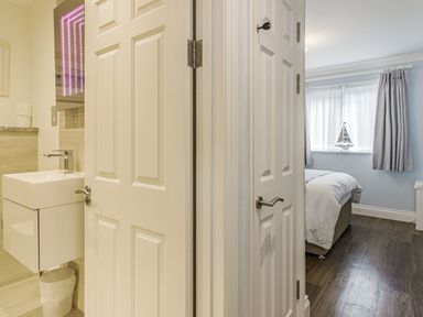 A view of a bathroom sink on the left and a bedroom with a bed and window on the right at Apartment 18 Burgh Island Causeway in Bigbury-On-Sea