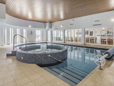 An indoor swimming pool with a circular hot tub and a seating area visible through glass windows at Apartment 18 Burgh Island Causeway in Bigbury-On-Sea