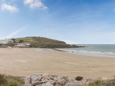 A sandy beach with some people near the water and a grassy hill with buildings in the background at Apartment 18 Burgh Island Causeway Bigbury-On-Sea