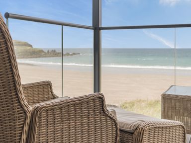 A wicker chair and table on a balcony with a view of the beach and sea at Apartment 18 Burgh Island Causeway in Bigbury-On-Sea