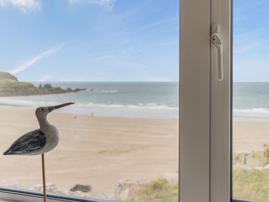 A window with a wooden bird decoration showing a beach and ocean view at Apartment 18 Burgh Island Causeway Bigbury-On-Sea