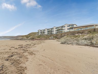 A sandy beach with tracks and seaweed near a cliff with a multi-story building on top at Apartment 18 Burgh Island Causeway Bigbury-On-Sea