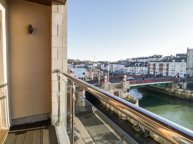 A balcony with glass and metal railing overlooking a river and a bridge with buildings along the riverbank at Townbridge Apartment in Weymouth
