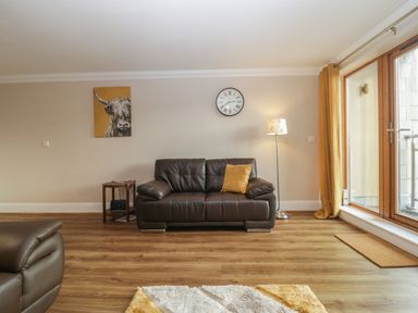 A living room with a brown leather sofa a side table with a radio a standing lamp a wall clock a yellow cushion a cow painting and large windows with yellow curtains at Townbridge Apartment in Weymouth
