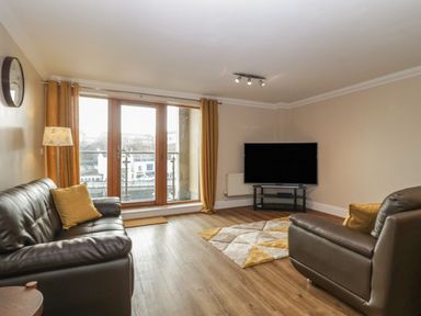A living room with leather sofas a TV on a stand and large windows with curtains at Townbridge Apartment in Weymouth