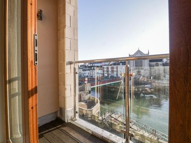 A small balcony with glass and metal railing overlooking a river and buildings at Townbridge Apartment in Weymouth