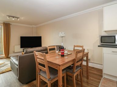 A dining table with four chairs a bottle of wine and wine glasses in a living room with a TV and leather sofas at Townbridge Apartment in Weymouth