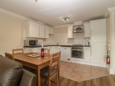 A kitchen with white cabinets a dining table with chairs a microwave toaster oven and wine bottle at Townbridge Apartment in Weymouth