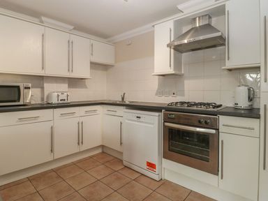 A kitchen with white cabinets black countertops a microwave toaster dishwasher oven stovetop and kettle at Townbridge Apartment in Weymouth