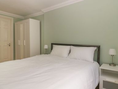 A bedroom with a bed with white bedding a white wardrobe and bedside tables with lamps at Townbridge Apartment in Weymouth