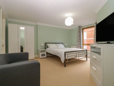 A bedroom with a bed a wardrobe a chair a television and a window at Townbridge Apartment in Weymouth