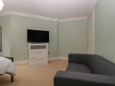 A room with a black couch a white chest of drawers with a television on top and part of a bed at Townbridge Apartment in Weymouth