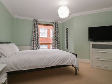 A bedroom with a bed a window patterned curtains a dresser with a television and a wall mirror at Townbridge Apartment in Weymouth