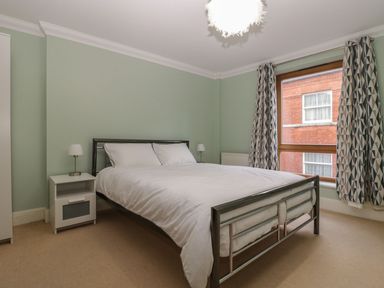 A bedroom with a metal framed double bed white bedding two bedside tables with lamps and a window with patterned curtains at Townbridge Apartment in Weymouth