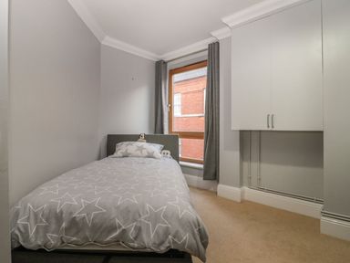A small bedroom with a single bed a window with curtains and wall cabinets at Townbridge Apartment in Weymouth