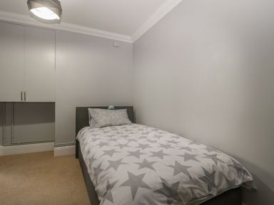 A bedroom with a single bed with star patterned bedding and a small cupboard above it at Townbridge Apartment in Weymouth