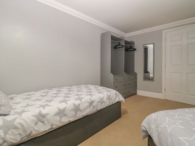 A bedroom with two single beds with star patterned bedding a grey wardrobe with hangers and a wall mirror at Townbridge Apartment in Weymouth