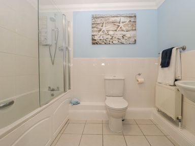 A bathroom with a bathtub and shower, toilet, towels on a radiator, and a picture of starfish on the wall at Townbridge Apartment in Weymouth