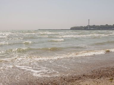 A shoreline with waves and pebbles and a distant pier with trees and a tall tower at Townbridge Apartment in Weymouth