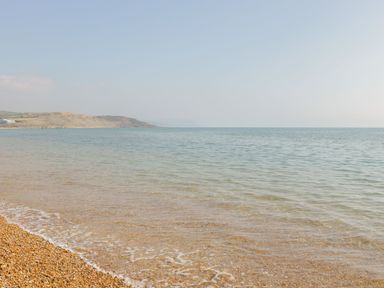 A pebbled beach with calm sea water and a distant coastline under a clear sky at Townbridge Apartment in Weymouth