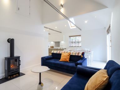 A living room with two blue sofas a small round table and a stove next to an open kitchen and dining area at Dreamwood Lodge in Keston near Leaves Green