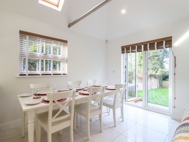A dining room with a white table set for six near windows and glass doors leading to a garden at Dreamwood Lodge in Keston near Leaves Green