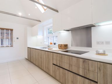 A kitchen with wooden lower cabinets white upper cabinets sink stove and a window at Dreamwood Lodge in Keston near Leaves Green
