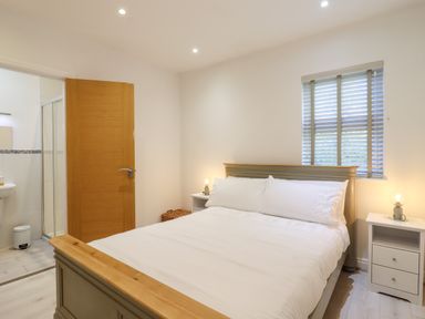 A bedroom with a double bed side tables with lamps wooden door and a window with blinds at Dreamwood Lodge in Keston near Leaves Green