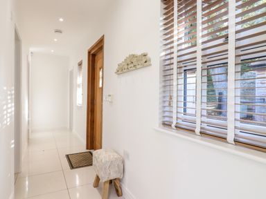A hallway with white walls a wooden door a small stool and blinds on a window at Dreamwood Lodge in Keston near Leaves Green