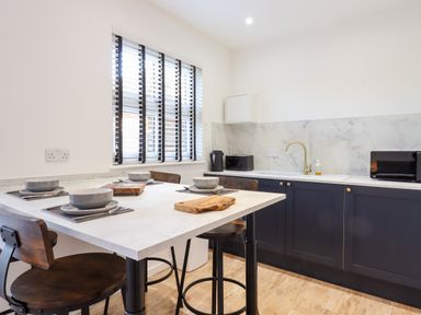 A kitchen with a white countertop dining table set for four and dark cabinets with appliances at Dreamwood Lodge in Keston near Leaves Green