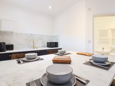 A kitchen with a marble countertop and backsplash set with bowls plates cutlery and a wooden chopping board at Dreamwood Lodge in Keston near Leaves Green