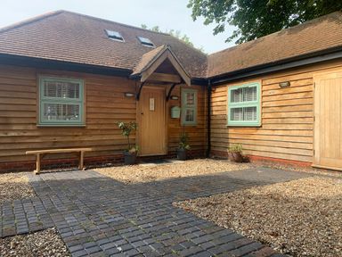A wooden exterior of a house with a paved walkway and potted plants at Dreamwood Lodge in Keston near Leaves Green