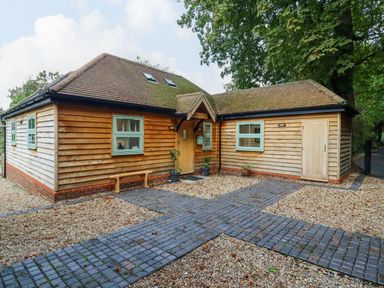 A wooden house with green window frames and a tiled roof with a brick and gravel driveway at Dreamwood Lodge in Keston near Leaves Green