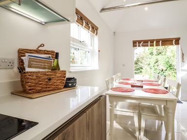 A kitchen dining area with a white table and chairs and a wicker basket with information pack at Dreamwood Lodge Keston near Leaves Green