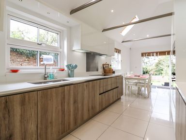 A kitchen with wooden cabinets a sink dining table and chairs and windows at Dreamwood Lodge in Keston near Leaves Green