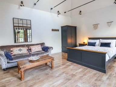 A bedroom with a gray bed and wardrobe a wooden coffee table and a gray velvet sofa with cushions at Dreamwood Lodge in Keston near Leaves Green