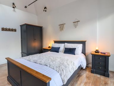 A bedroom with a bed flanked by two nightstands and a wardrobe against a wall at Dreamwood Lodge in Keston near Leaves Green