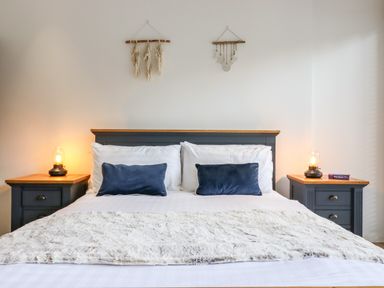 A bedroom with a double bed two bedside tables with lamps and wall hangings at Dreamwood Lodge in Keston near Leaves Green