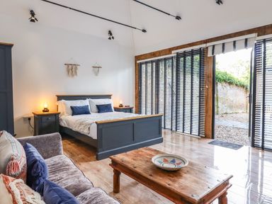 A bedroom with a bed sofa wooden table and large windows with blinds at Dreamwood Lodge in Keston near Leaves Green