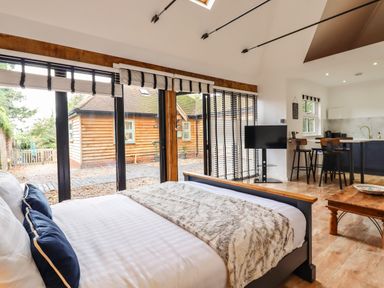 A bedroom with a bed in front of large windows next to a kitchen area with bar stools and a TV at Dreamwood Lodge in Keston near Leaves Green