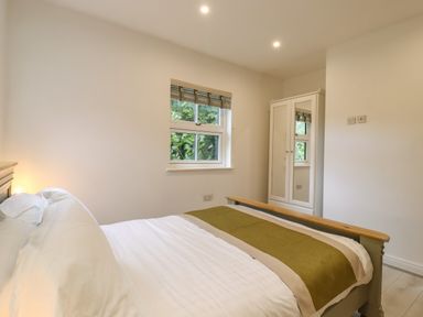 A bedroom with a bed with white bedding a green throw a window with blinds and a wardrobe at Dreamwood Lodge in Keston near Leaves Green