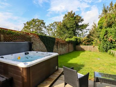A backyard with a hot tub a rubber duck two chairs and a glass table surrounded by trees and a brick wall at Dreamwood Lodge in Keston near Leaves Green
