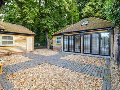 An outdoor courtyard with two wooden buildings surrounded by trees at Dreamwood Lodge in Keston near Leaves Green