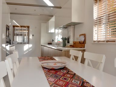 A kitchen with white chairs around a table with a patterned runner and a wicker basket at Dreamwood Lodge in Keston near Leaves Green