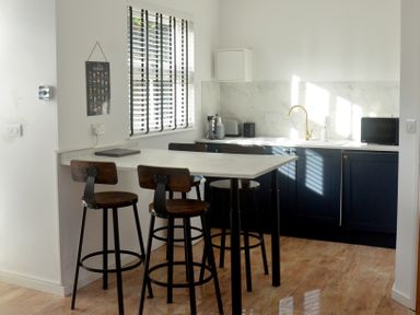 A kitchen with a marble island and bar stools near a window with blinds at Dreamwood Lodge in Keston near Leaves Green