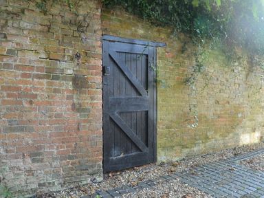 A black wooden door set in a brick wall with ivy hanging above and a gravel and stone pathway