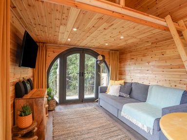 A living room with a gray sofa and wooden walls and ceiling and round black framed glass doors at The Hideaway Pod in Rhoslan near Criccieth