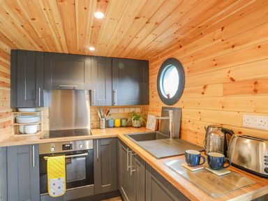 A kitchen with wooden walls dark cabinets an oven sink and two blue mugs at The Hideaway Pod in Rhoslan near Criccieth
