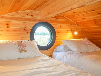 A bedroom with two beds and a round window in a wooden pod at The Hideaway Pod in Rhoslan near Criccieth
